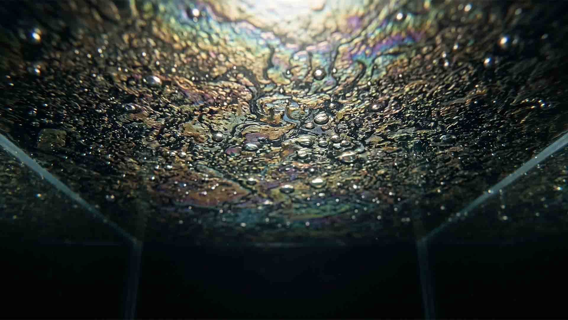 Under-water macro angle of a thick oily protein biofilm floating on stagnant aquarium water surface blocking oxygen.